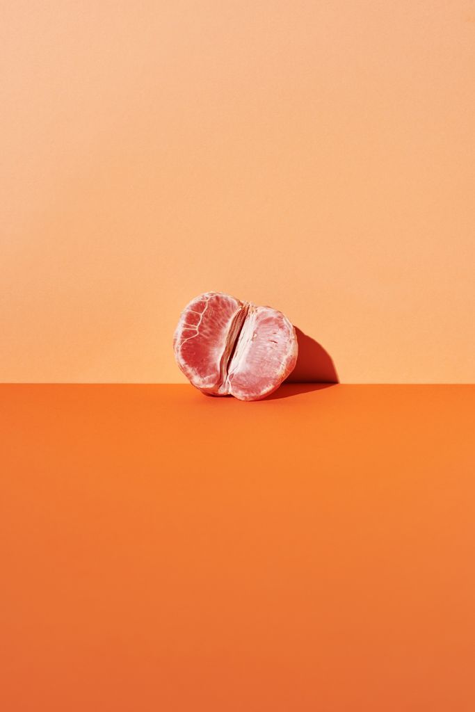 Artistic minimalist photo of a half-peeled pomelo on a two-tone orange background.